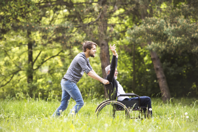 old man assisted by his son pushing the wheelchair